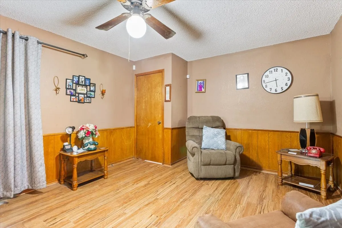 Living area with wood finished floors, a textured ceiling, wood walls, a ceiling fan, and a wainscoted wall