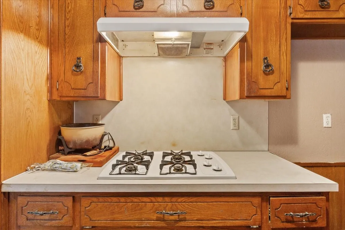 Kitchen with light countertops, under cabinet range hood, brown cabinets, white gas stovetop, and wood walls