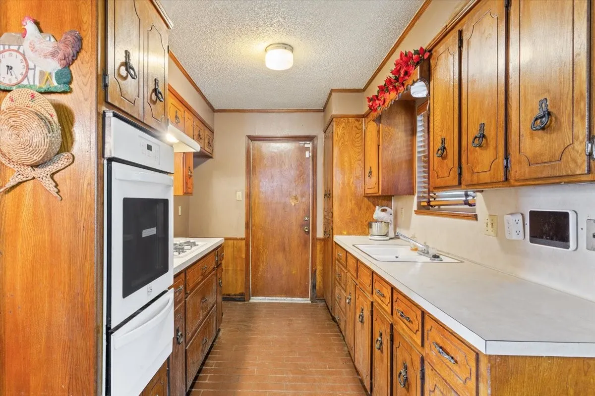 Kitchen with light countertops, brown cabinets, a textured ceiling, a warming drawer, and oven