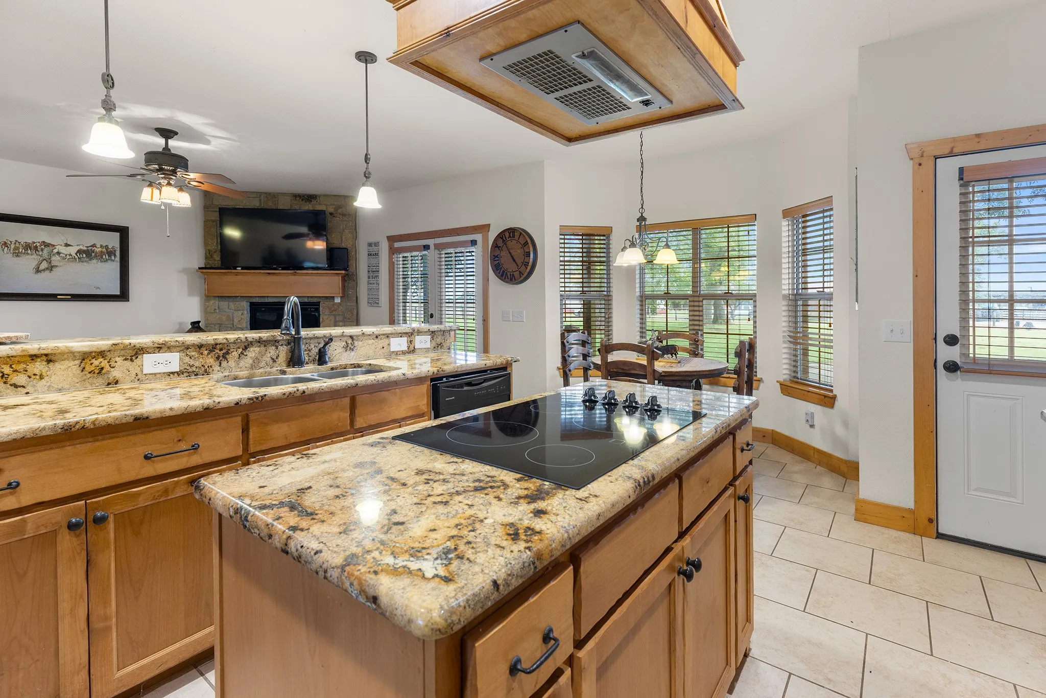 Kitchen with range hood, pendant lighting, light stone counters, and brown cabinets