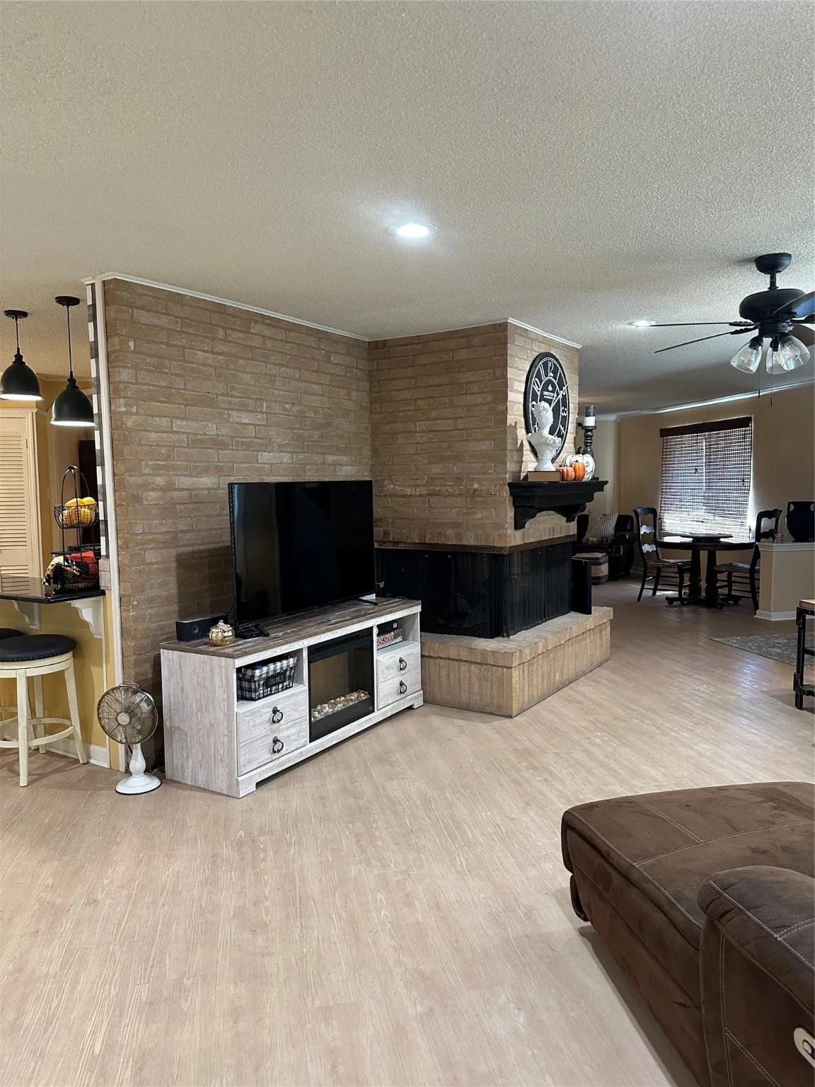 Living room with a textured ceiling, light wood-style flooring, a ceiling fan, and a fireplace