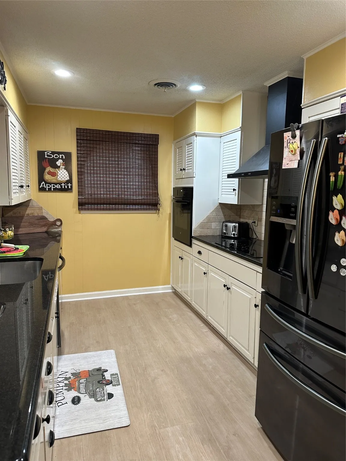 Kitchen featuring fridge, a textured ceiling, light wood-style flooring, black oven, and ornamental molding