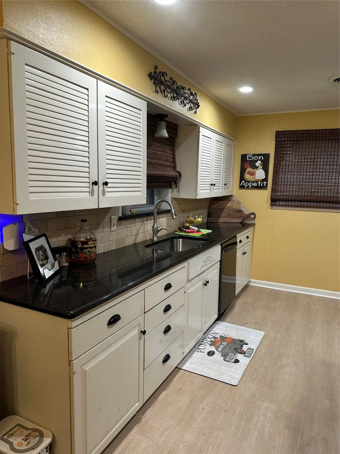 Kitchen with a textured ceiling, light wood-type flooring, dark stone countertops, tasteful backsplash, and dishwasher