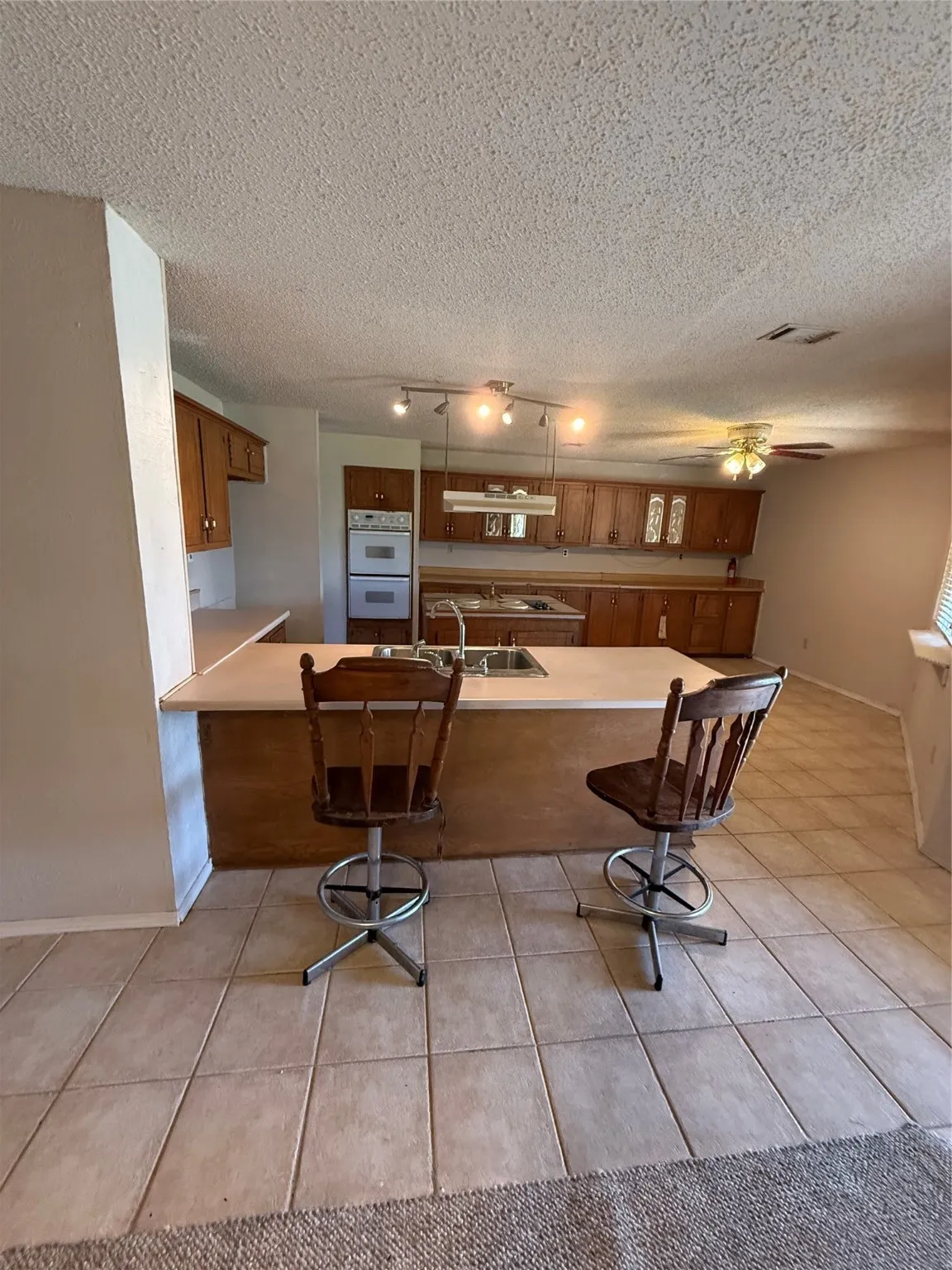 Kitchen featuring brown cabinets, a kitchen bar, light countertops, light tile patterned floors, and a peninsula