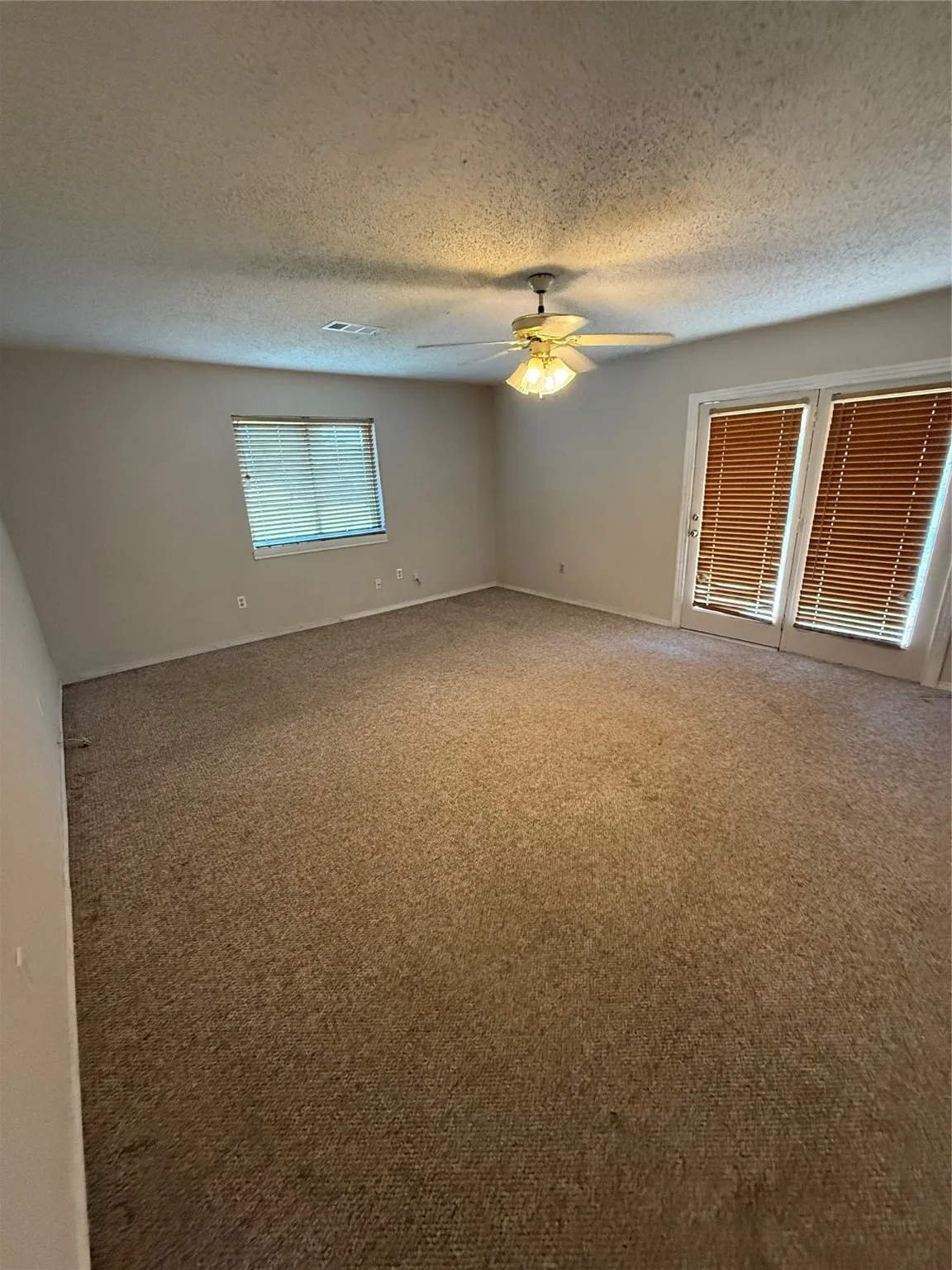 Empty room featuring carpet floors, a textured ceiling, and a ceiling fan