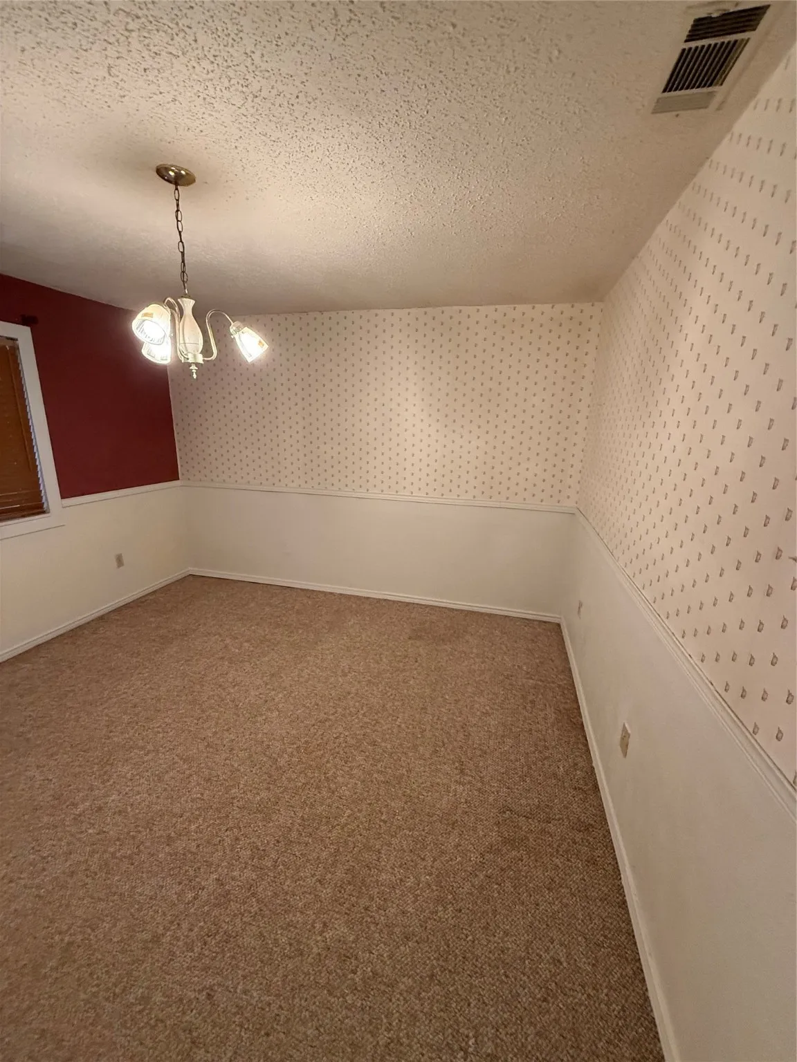 Carpeted spare room featuring a textured ceiling, a chandelier, and wallpapered walls