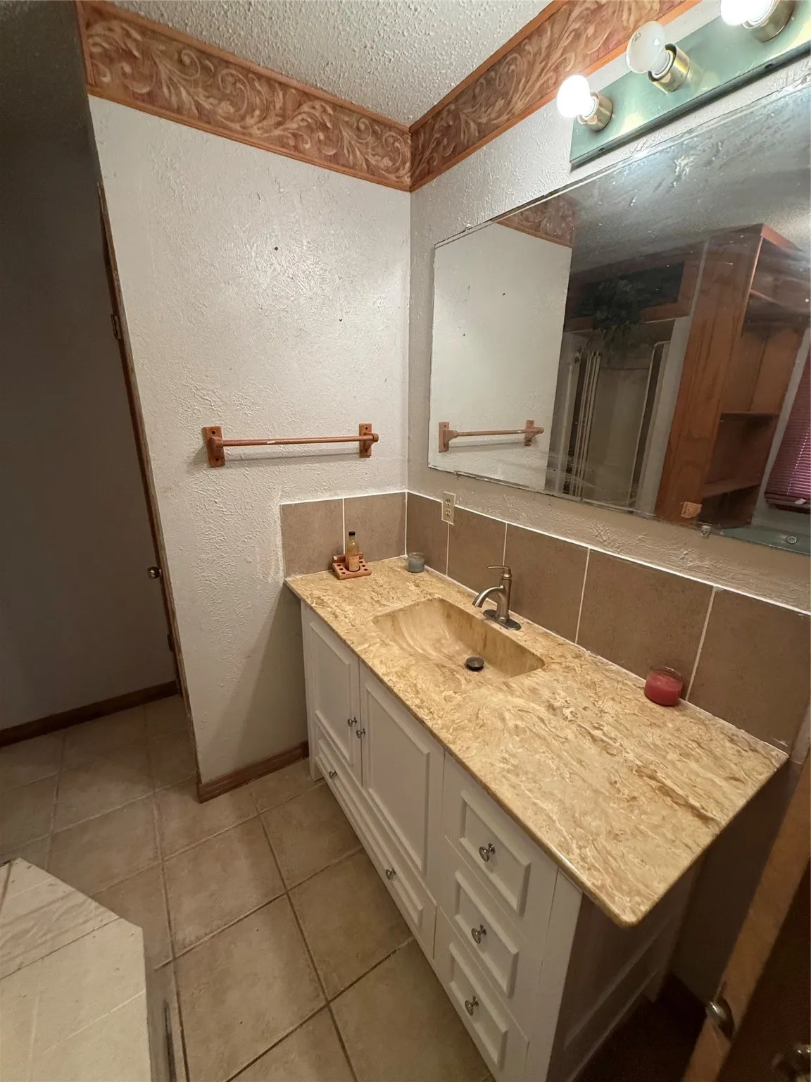 Full bath with a textured wall, vanity, decorative backsplash, a textured ceiling, and light tile patterned flooring