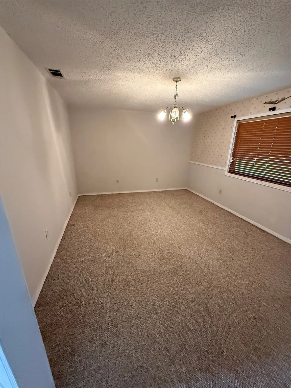 Empty room featuring a textured ceiling and a chandelier