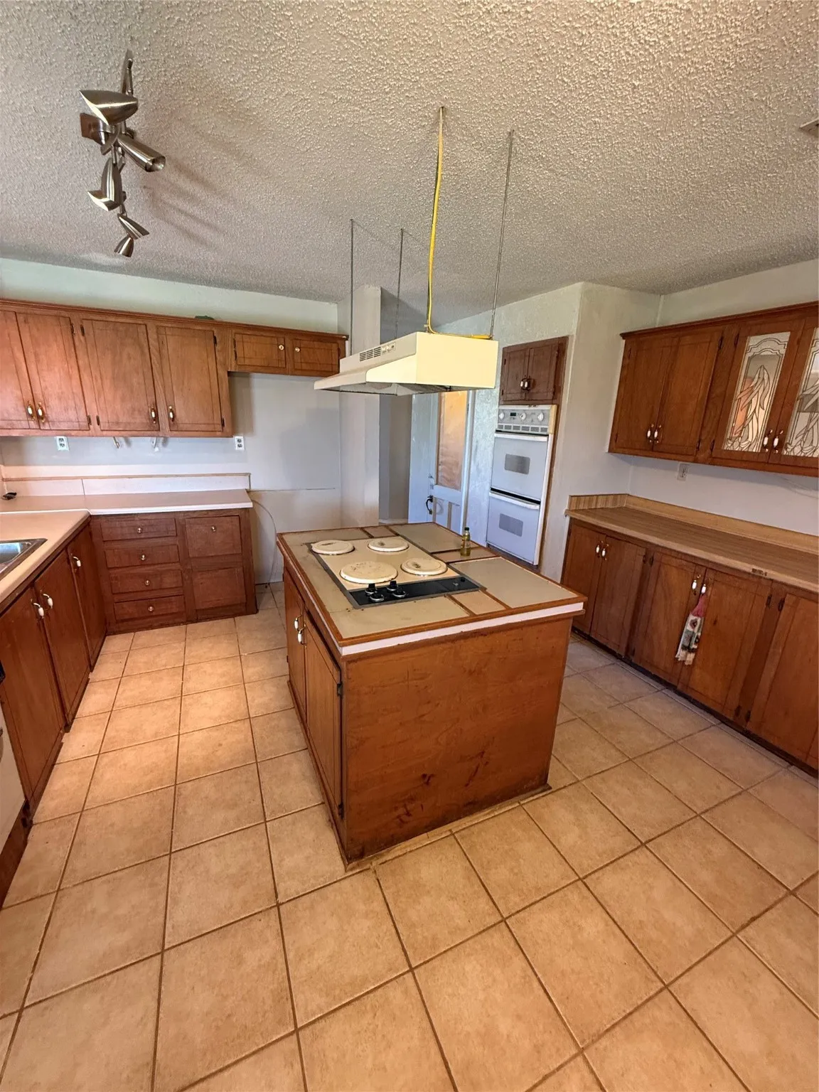 Kitchen featuring a textured ceiling, a kitchen island, light tile patterned floors, brown cabinets, and light countertops