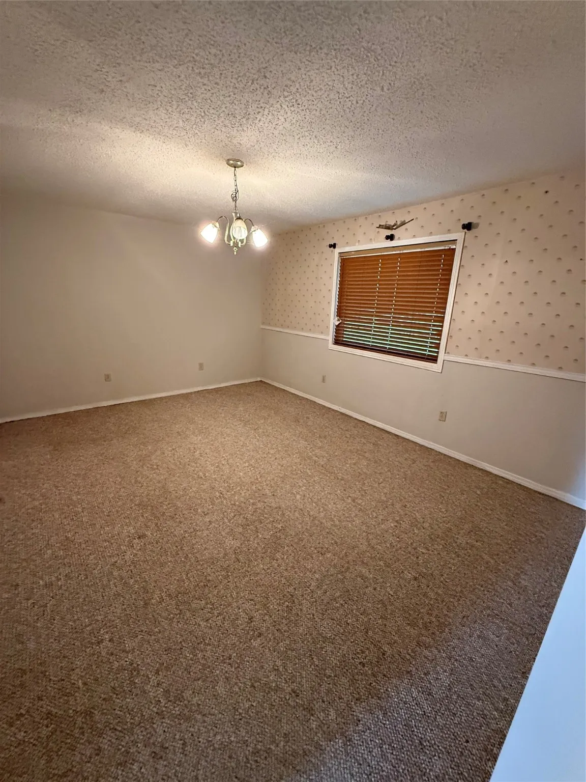 Carpeted spare room featuring a textured ceiling, a chandelier, and wallpapered walls