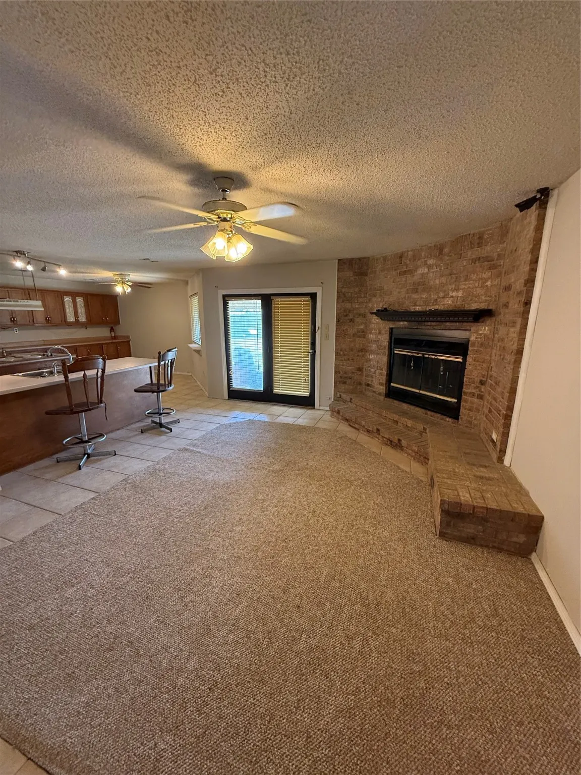 Living room with light tile patterned flooring, a textured ceiling, a brick fireplace, and light colored carpet