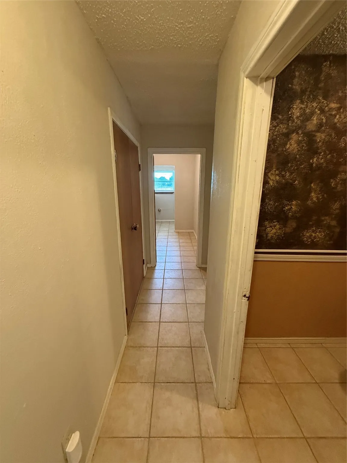 Corridor with light tile patterned floors and a textured ceiling