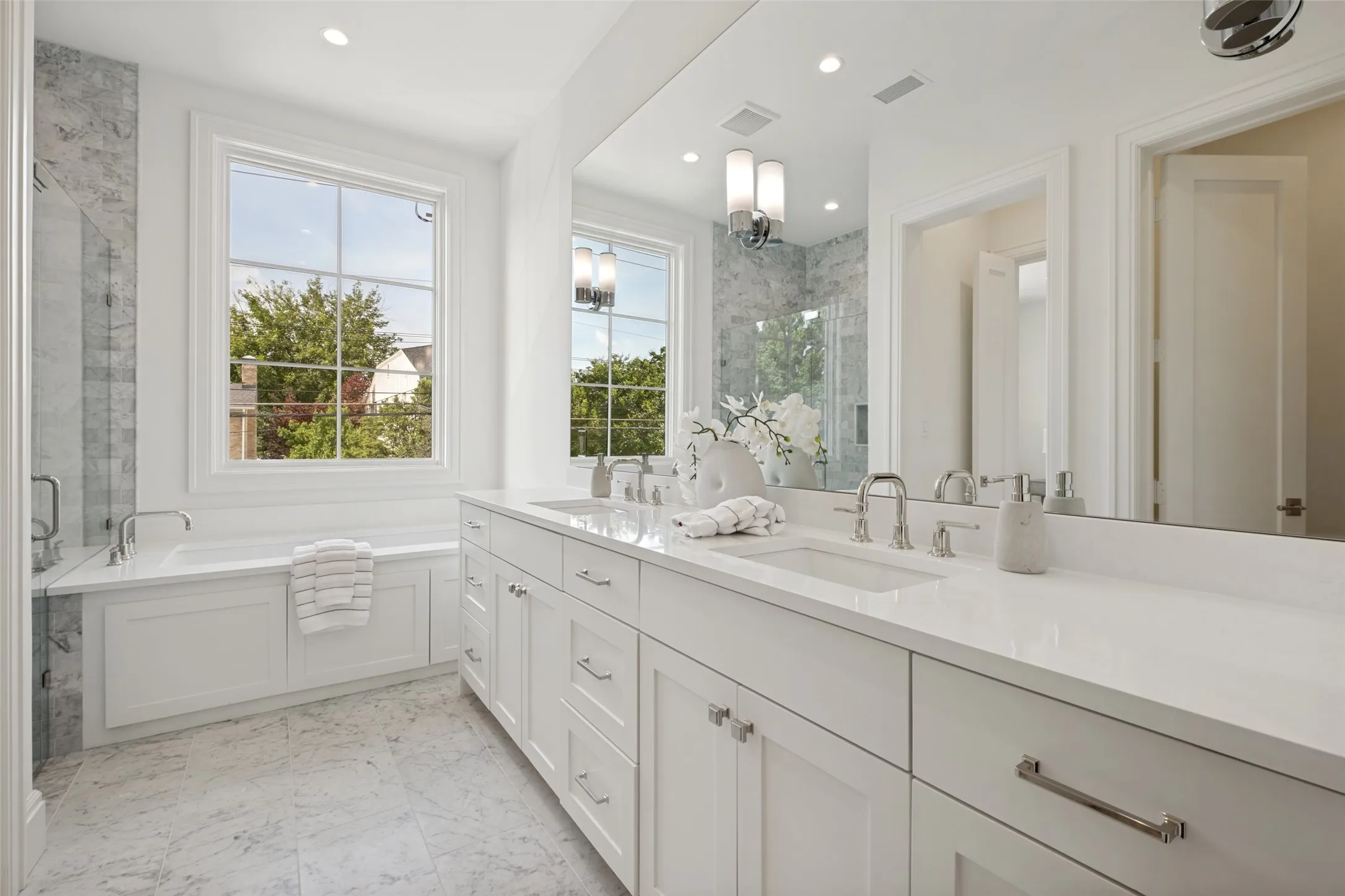Luxurious primary ensuite featuring designer surfaces, high-end hardware, dual vanities, and a separate soaking tub and walk-in shower.