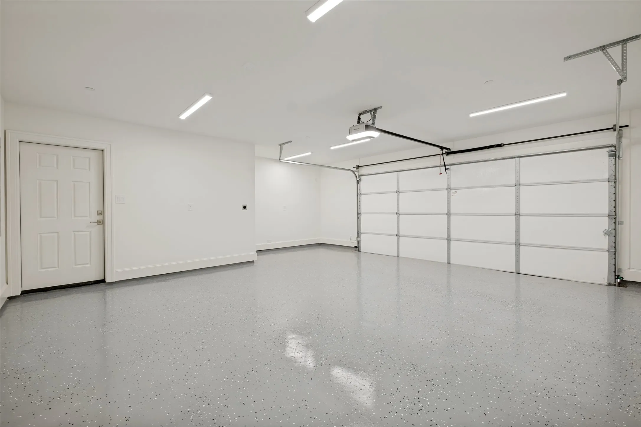 Spacious rear-entry two-car garage featuring an epoxy-coated floor, a dedicated storage nook, and a side-yard access door.