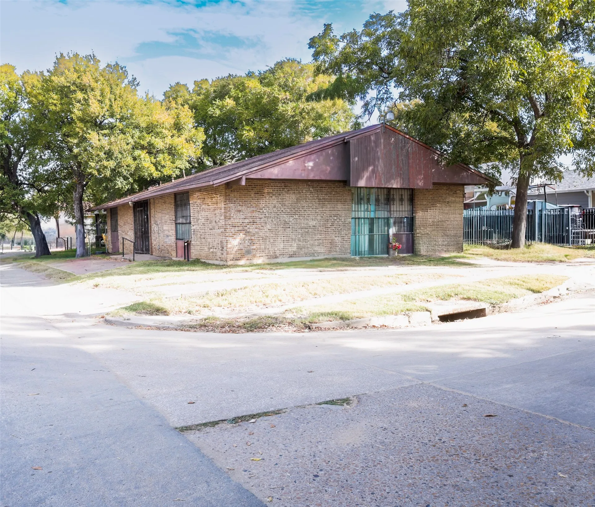 Brick exterior structure with a pitched roof, featuring mature trees and a paved street
