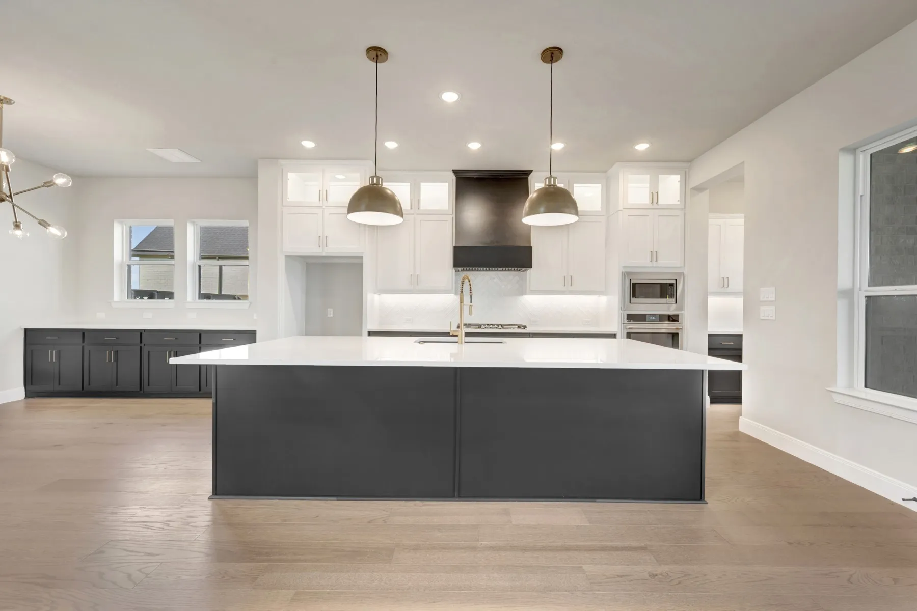 Kitchen with dual tone cabinetry, glass insert cabinets, light wood finished floors, a large island with sink, and pendant lighting