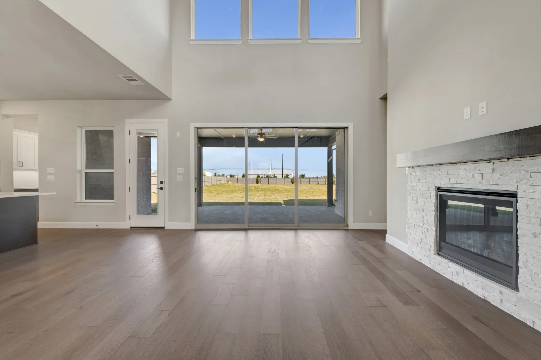 Unfurnished living room featuring a stone fireplace, dark wood-style flooring, and a high ceiling