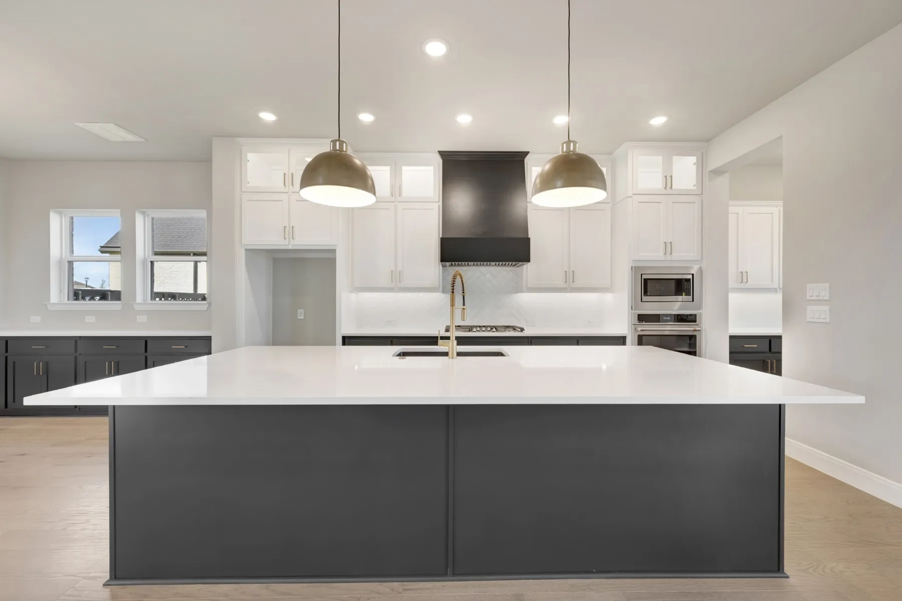 Two tone kitchen with dual tone cabinets, a large island, glass fronted cabinets, stainless steel appliances, and light stone countertops