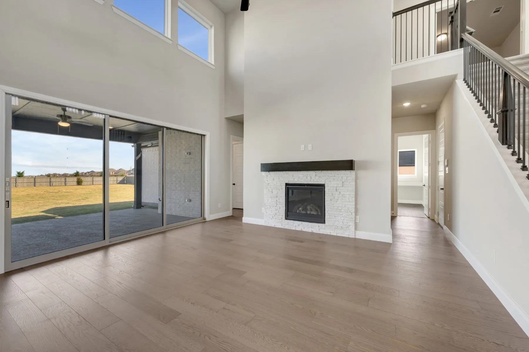 Unfurnished living room with wood finished floors, a high ceiling, a stone fireplace, and a ceiling fan