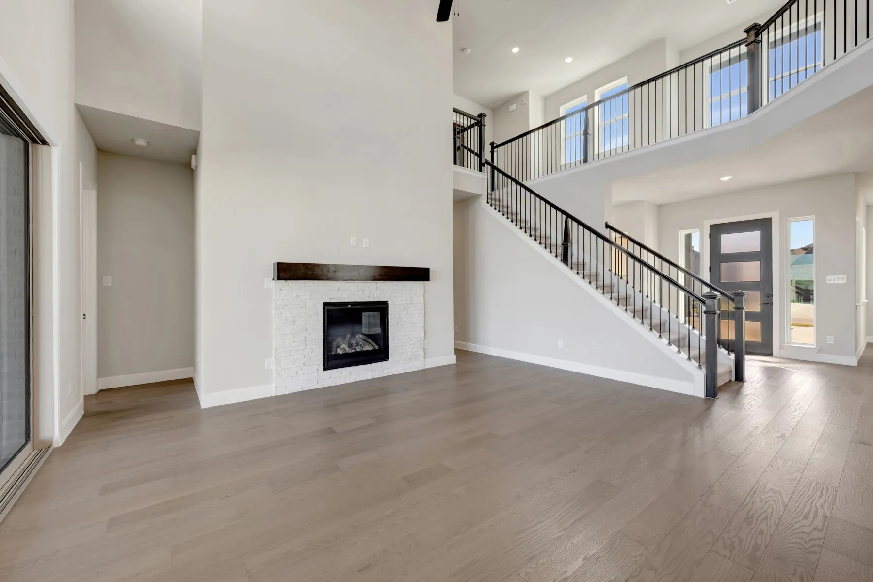 Unfurnished living room featuring wood finished floors, a high ceiling, a stone fireplace, and recessed lighting