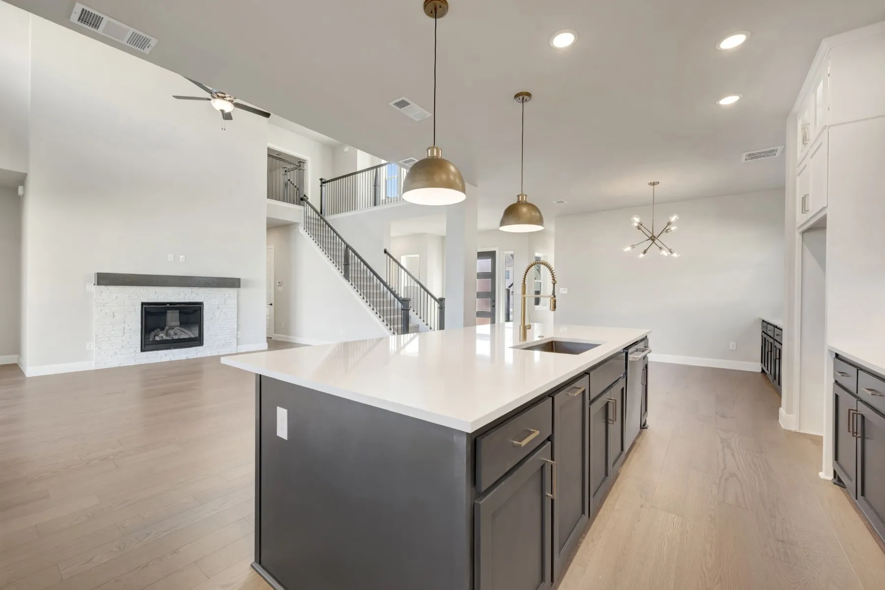 Kitchen featuring open floor plan, light wood-style flooring, a chandelier, a stone fireplace, and a kitchen island with sink