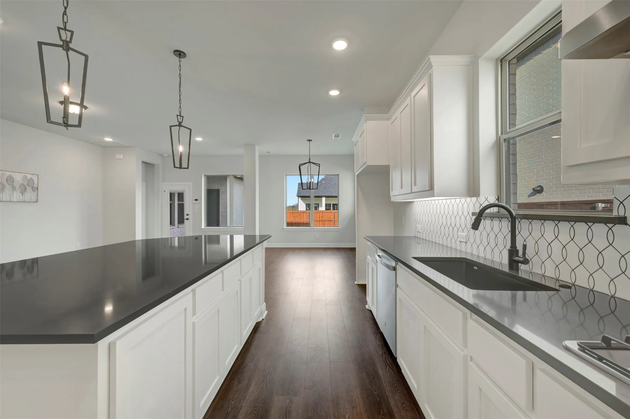 Kitchen featuring white cabinets, dark wood finished floors, pendant lighting, dishwasher, and dark stone counters