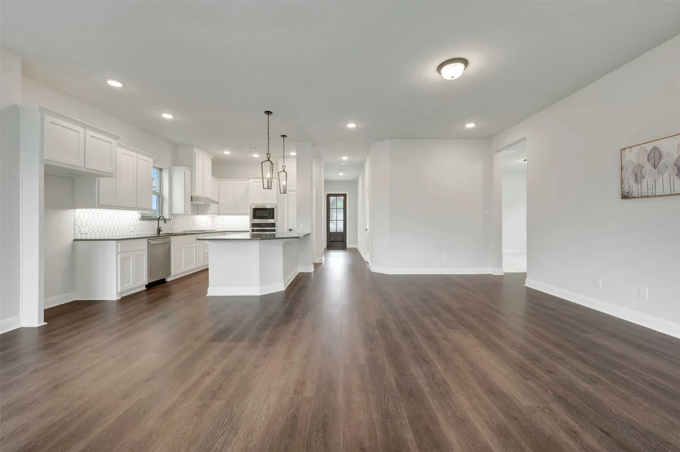 Kitchen with open floor plan, white cabinetry, dark wood-type flooring, and stainless steel dishwasher