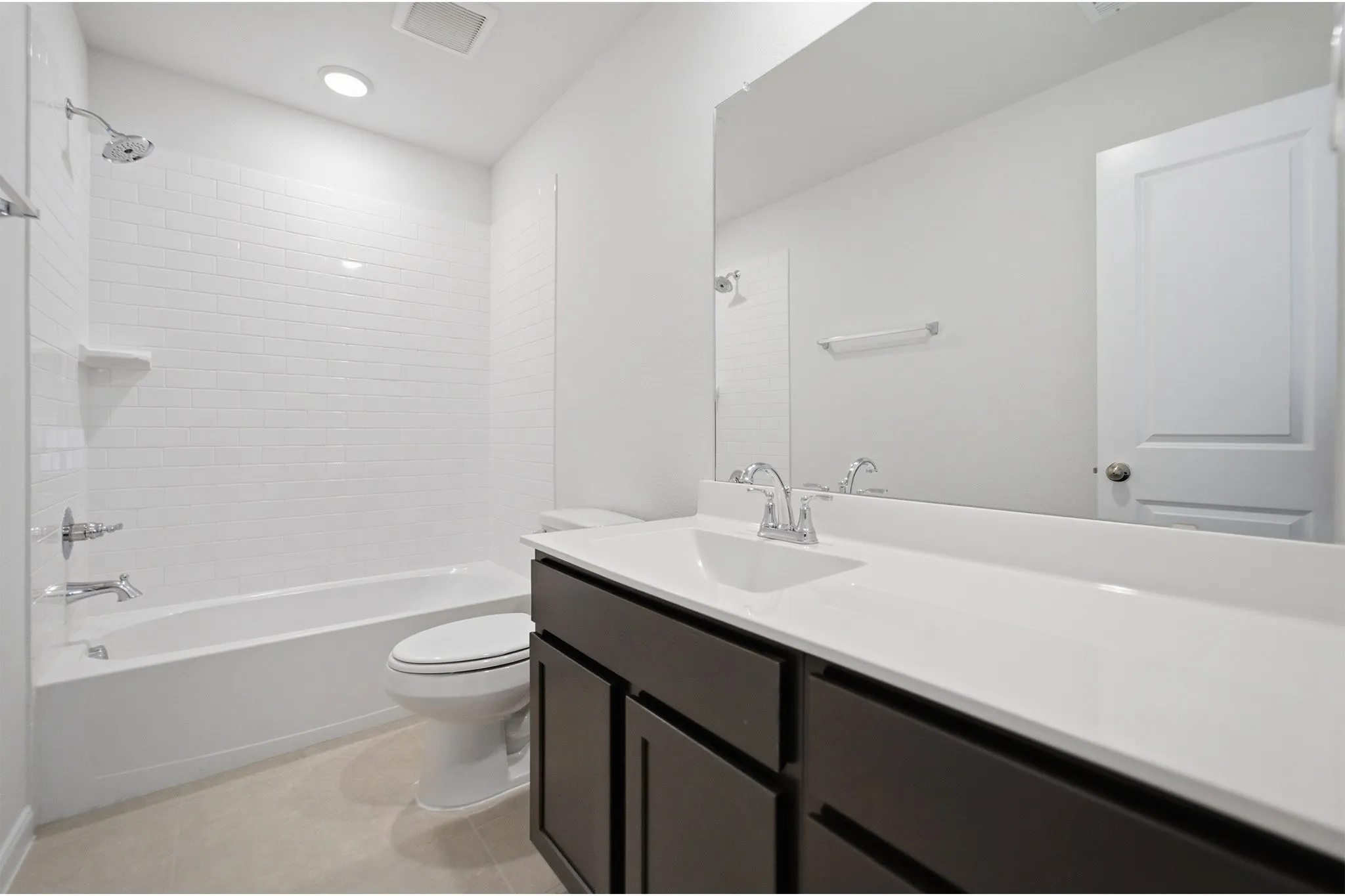Bathroom featuring a white subway tile tub surround, chrome fixtures, dark wood-finish vanity with a white countertop, and an integrated rectangular sink