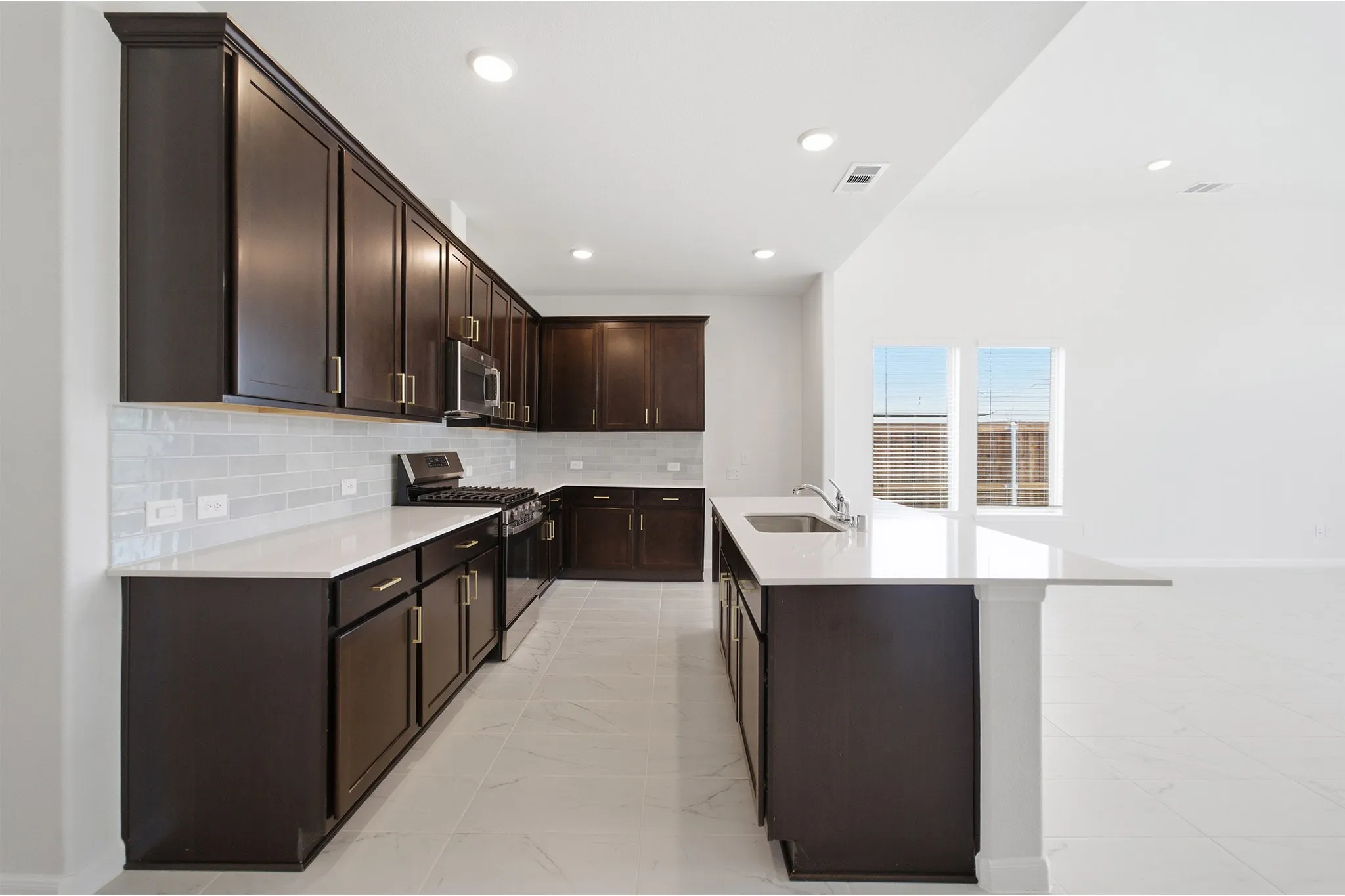 Open-concept kitchen featuring dark wood cabinetry, white countertops, subway tile backsplash, stainless steel appliances, and a kitchen island with an integrated sink