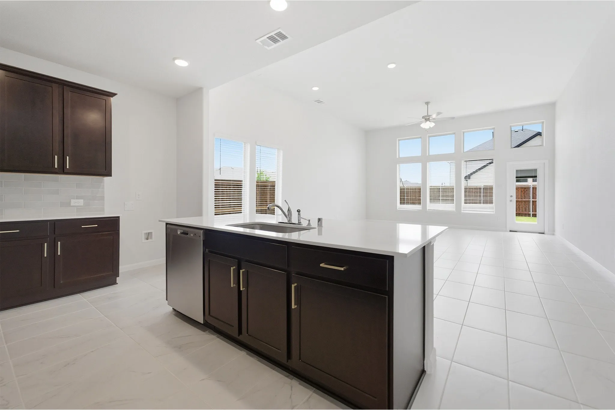 Open-concept kitchen featuring dark wood cabinetry, white countertops, subway tile backsplash, stainless steel appliances, and a kitchen island with an integrated sink