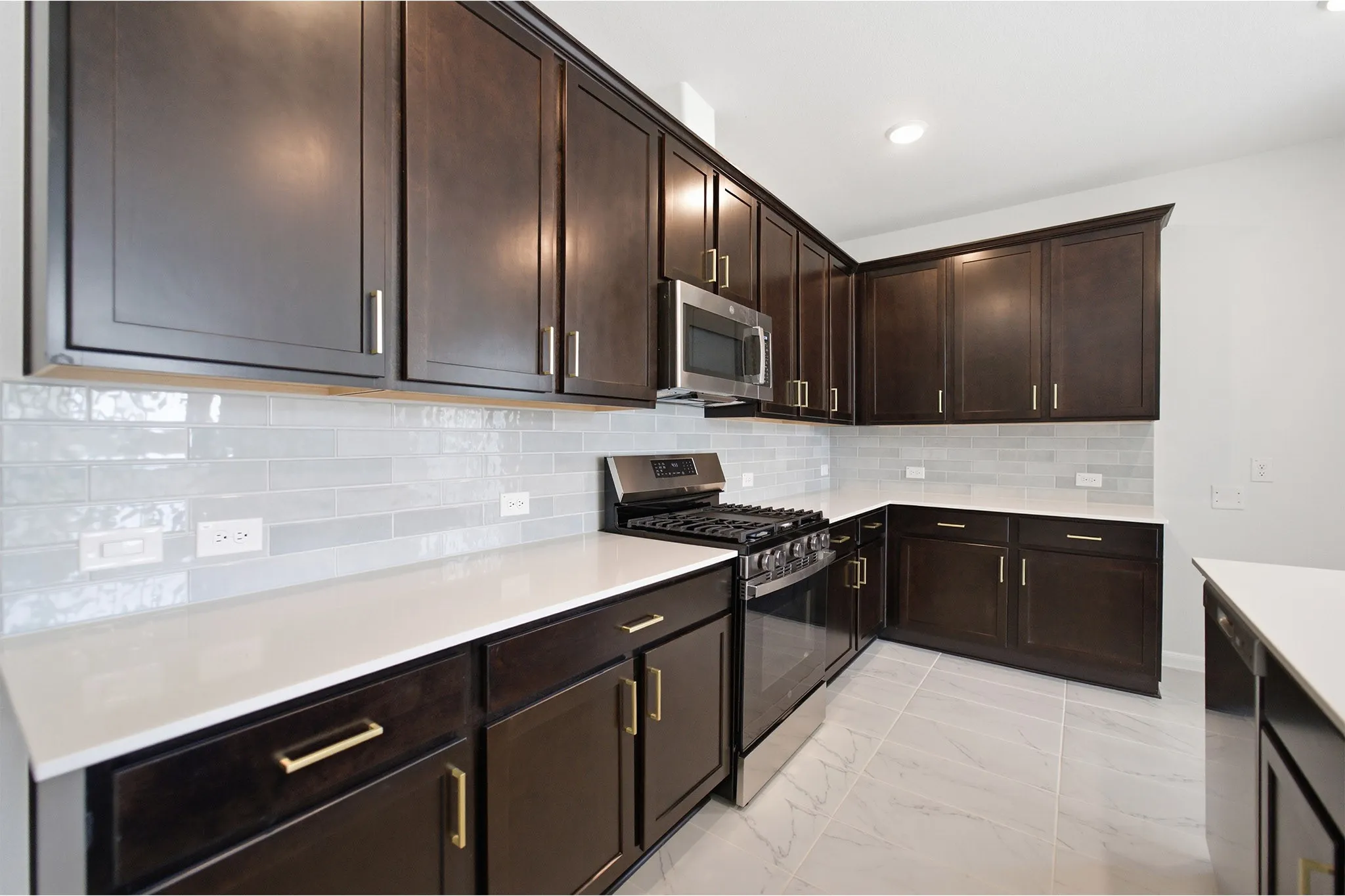 Corner kitchen featuring dark wood cabinetry, light countertops, subway tile backsplash, stainless steel appliances, and tile flooring