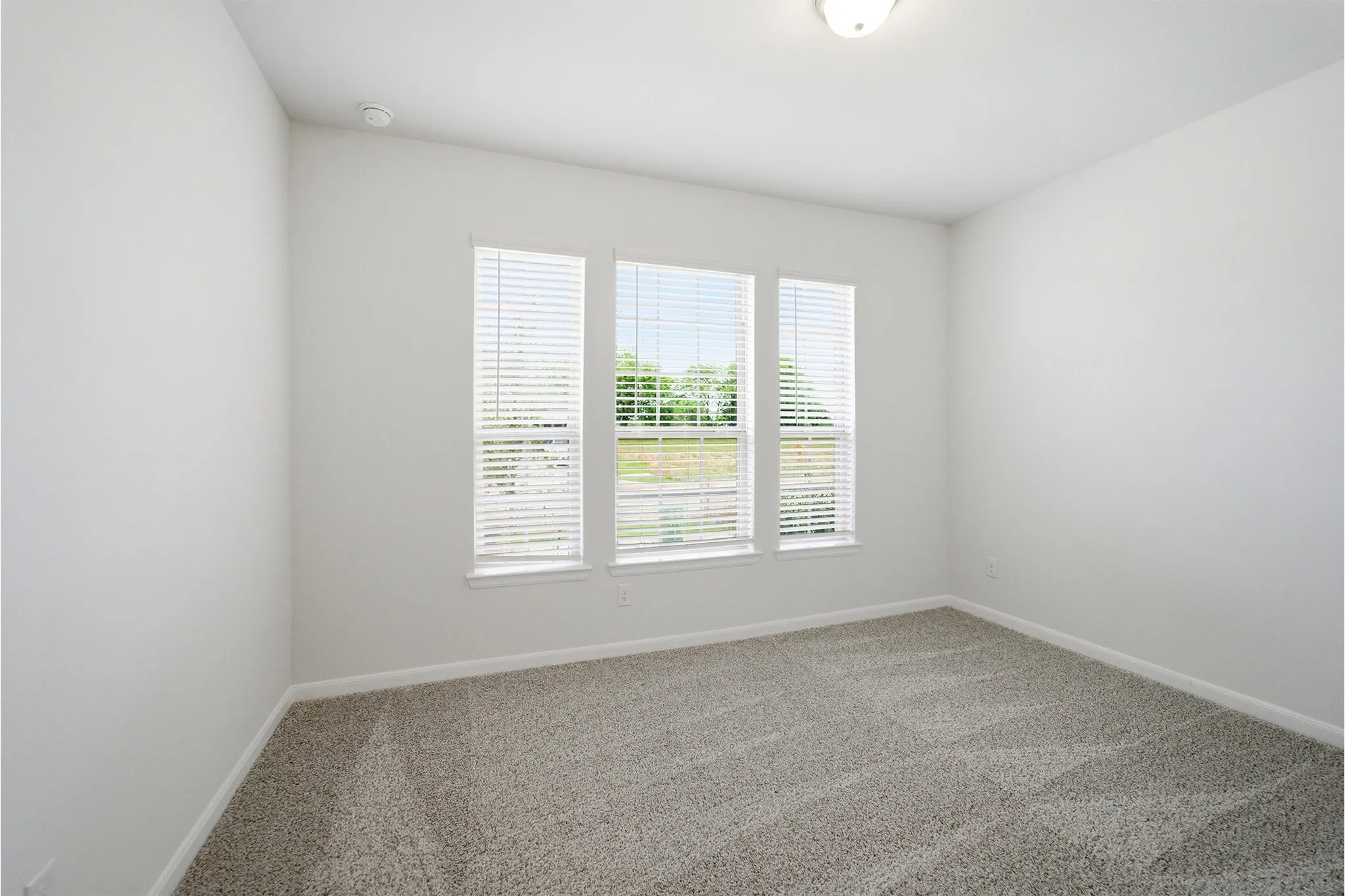 Room featuring three windows with blinds, light gray wall paint, and gray patterned carpet flooring