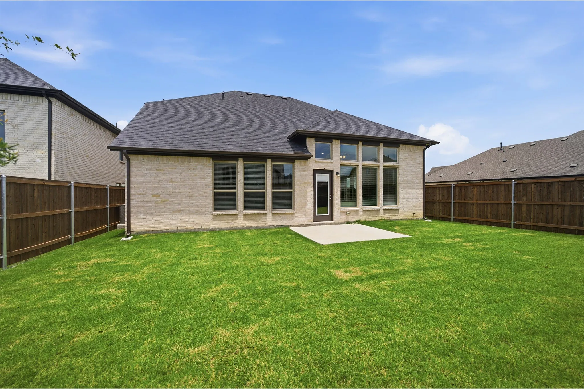 Spacious rear yard featuring a concrete patio, light-colored brick exterior, dark-framed windows, and a dark shingle roof