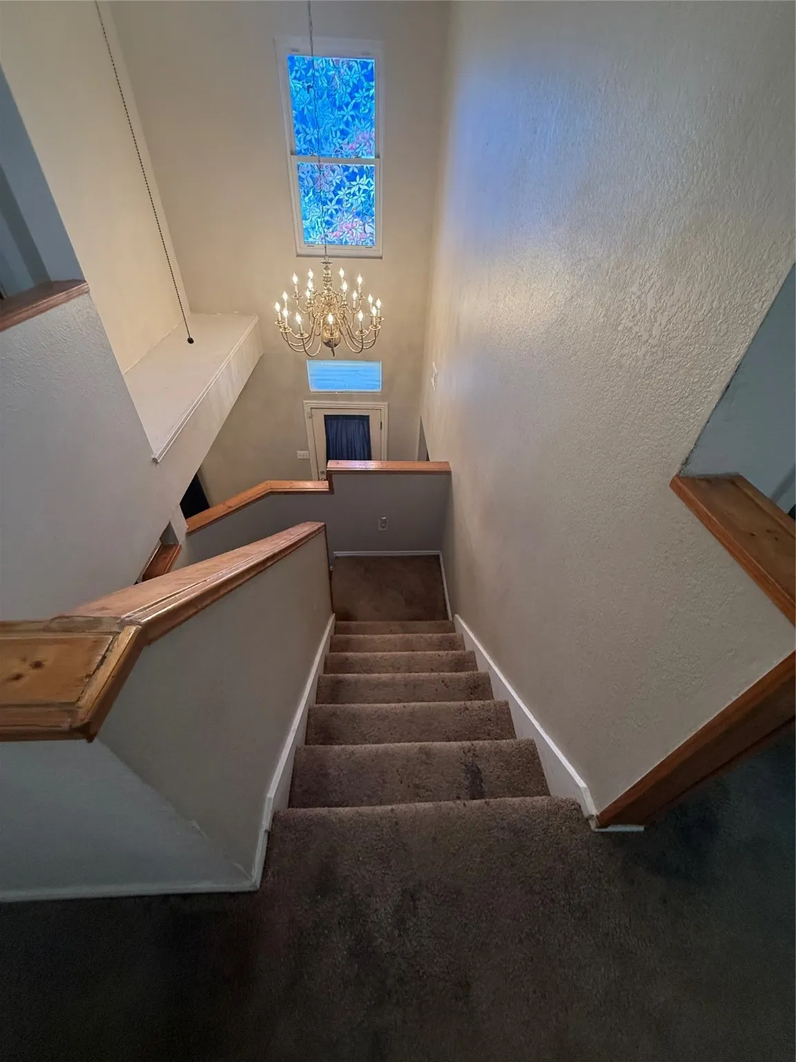 Stairs featuring carpet floors, a textured wall, and a chandelier