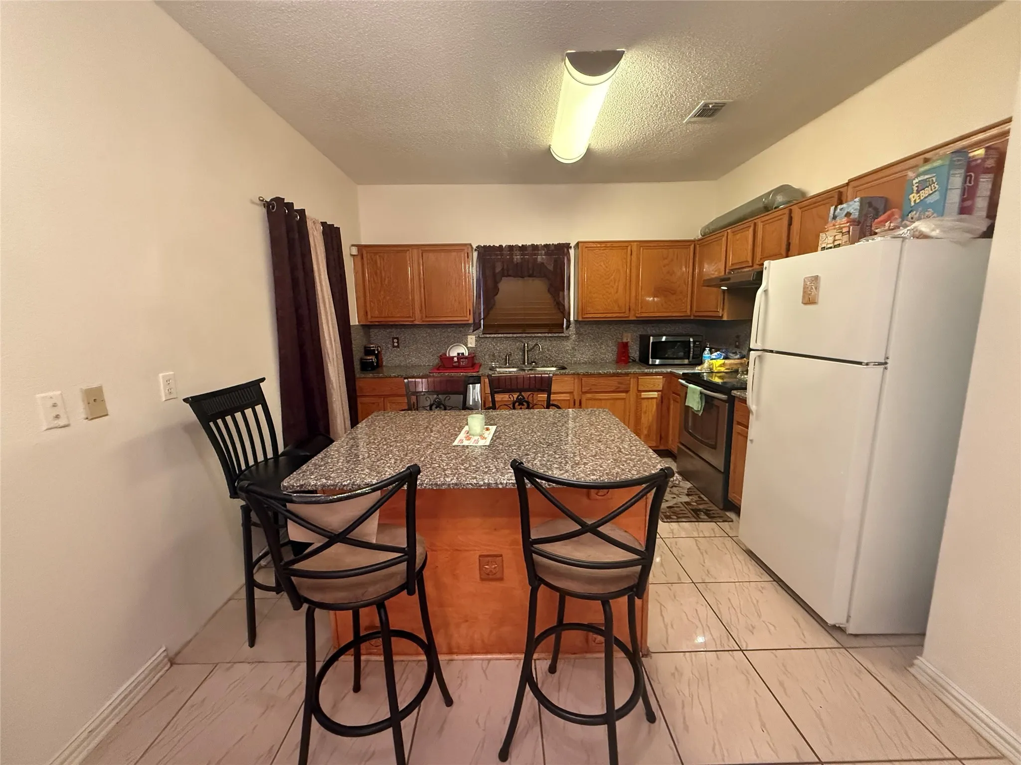 Kitchen featuring appliances with stainless steel finishes, brown cabinetry, backsplash, dark stone countertops, and a textured ceiling