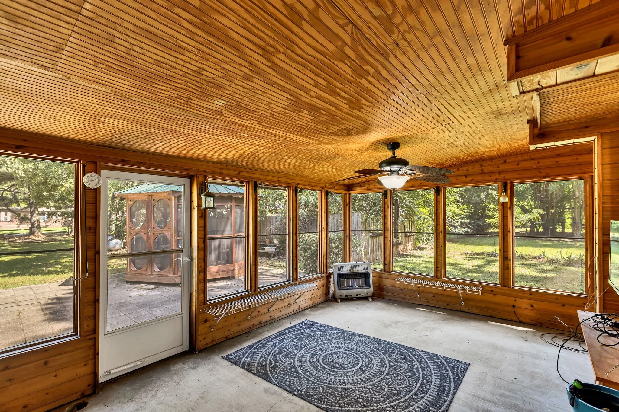 Sunroom featuring heating unit, roll up shades with screens and a ceiling fan