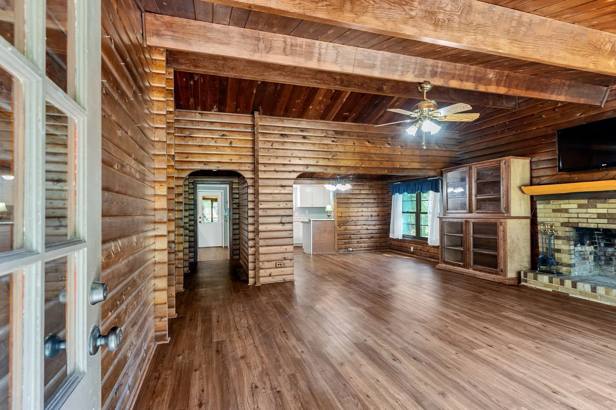 Living room featuring rustic walls, hardwood / wood-style flooring, a brick fireplace, a wood ceiling with exposed beams, and a ceiling fan