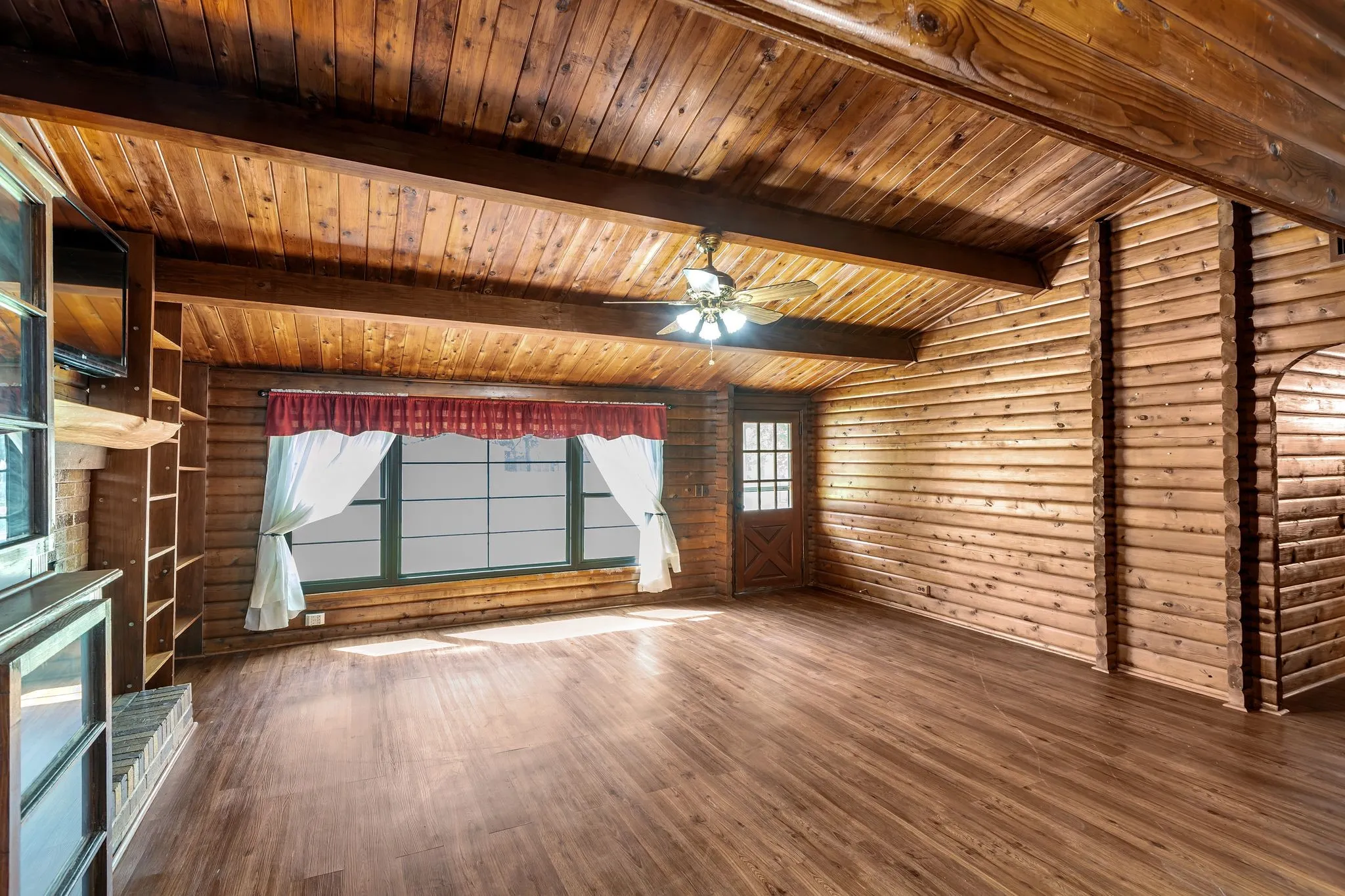 Living room featuring log walls, dark wood-style floors, wooden ceiling, and a ceiling fan