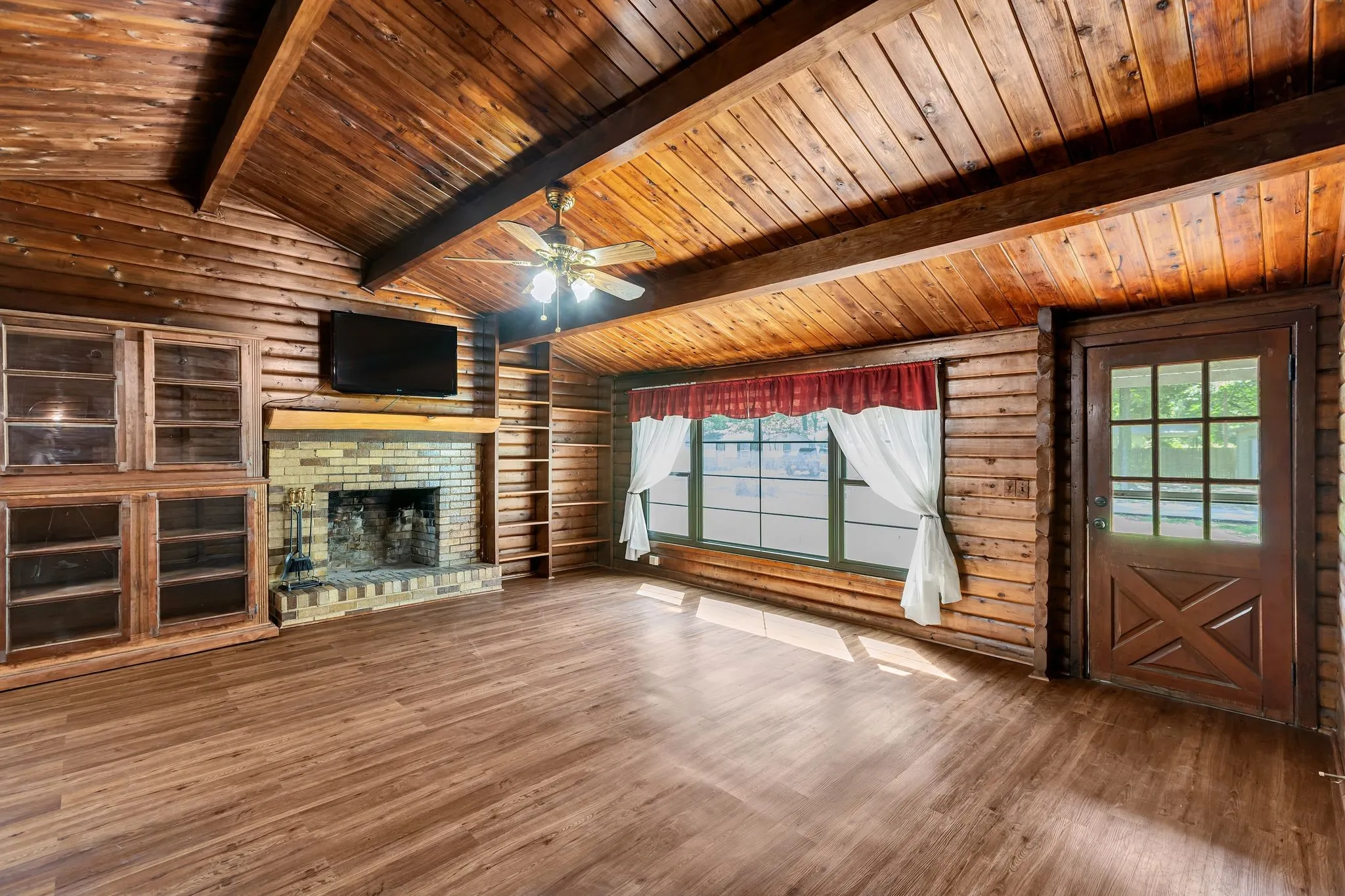 iving room with a brick fireplace, wood finished floors, a ceiling fan, rustic walls, and wood ceiling