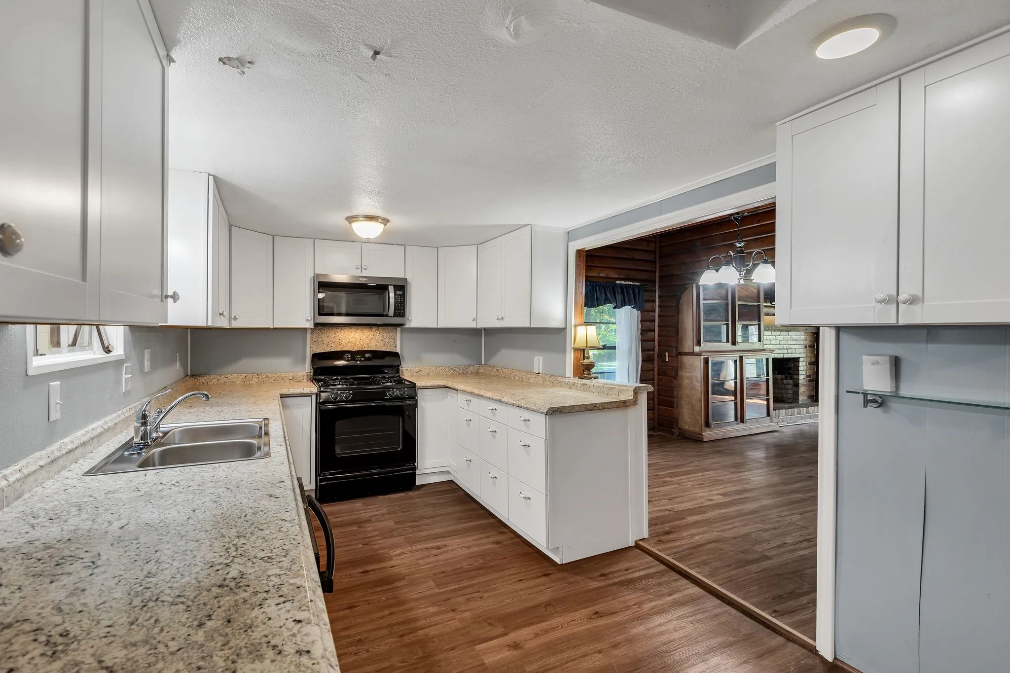 Kitchen with black range, dark wood-style floors, white cabinets, stainless steel microwave