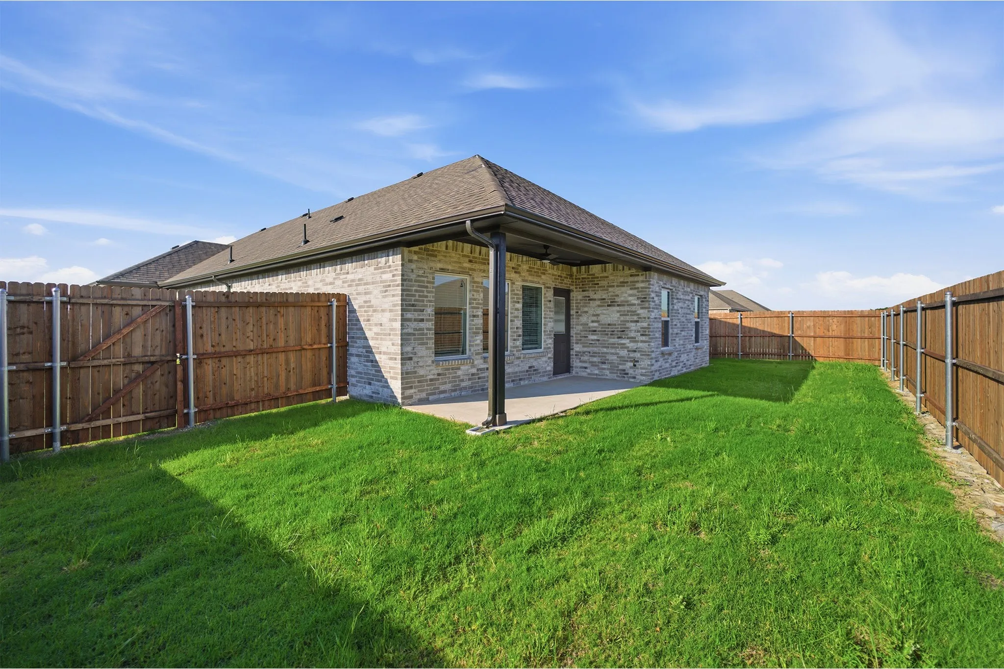 Private backyard featuring a covered concrete patio, wood fencing, and a mature lawn