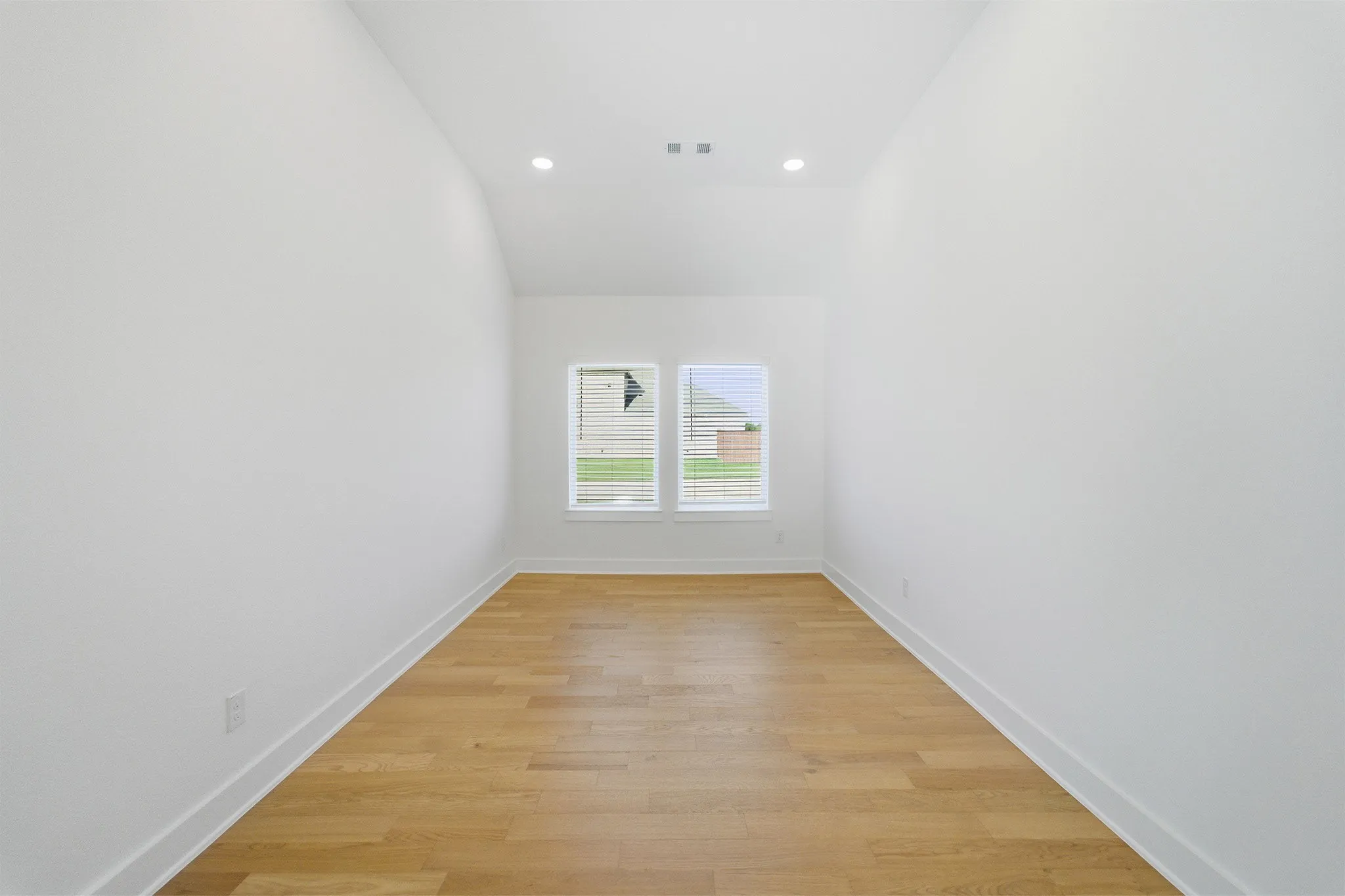 Recessed lighting illuminates the room, featuring wood-finish flooring and white baseboards