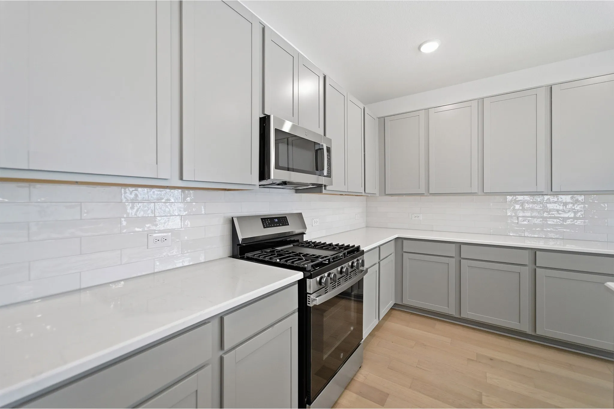 Contemporary kitchen featuring light gray cabinetry, white countertops, a subway tile backsplash, stainless steel appliances, and light wood-finish flooring