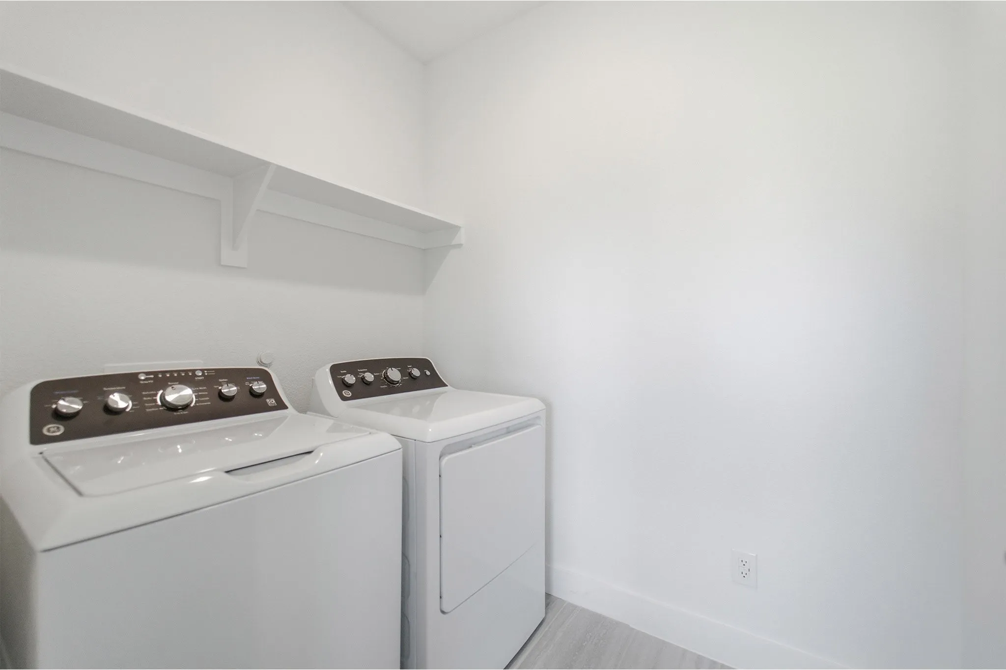 Dedicated laundry area featuring white walls, a white wall-mounted shelf, and light wood-finish flooring