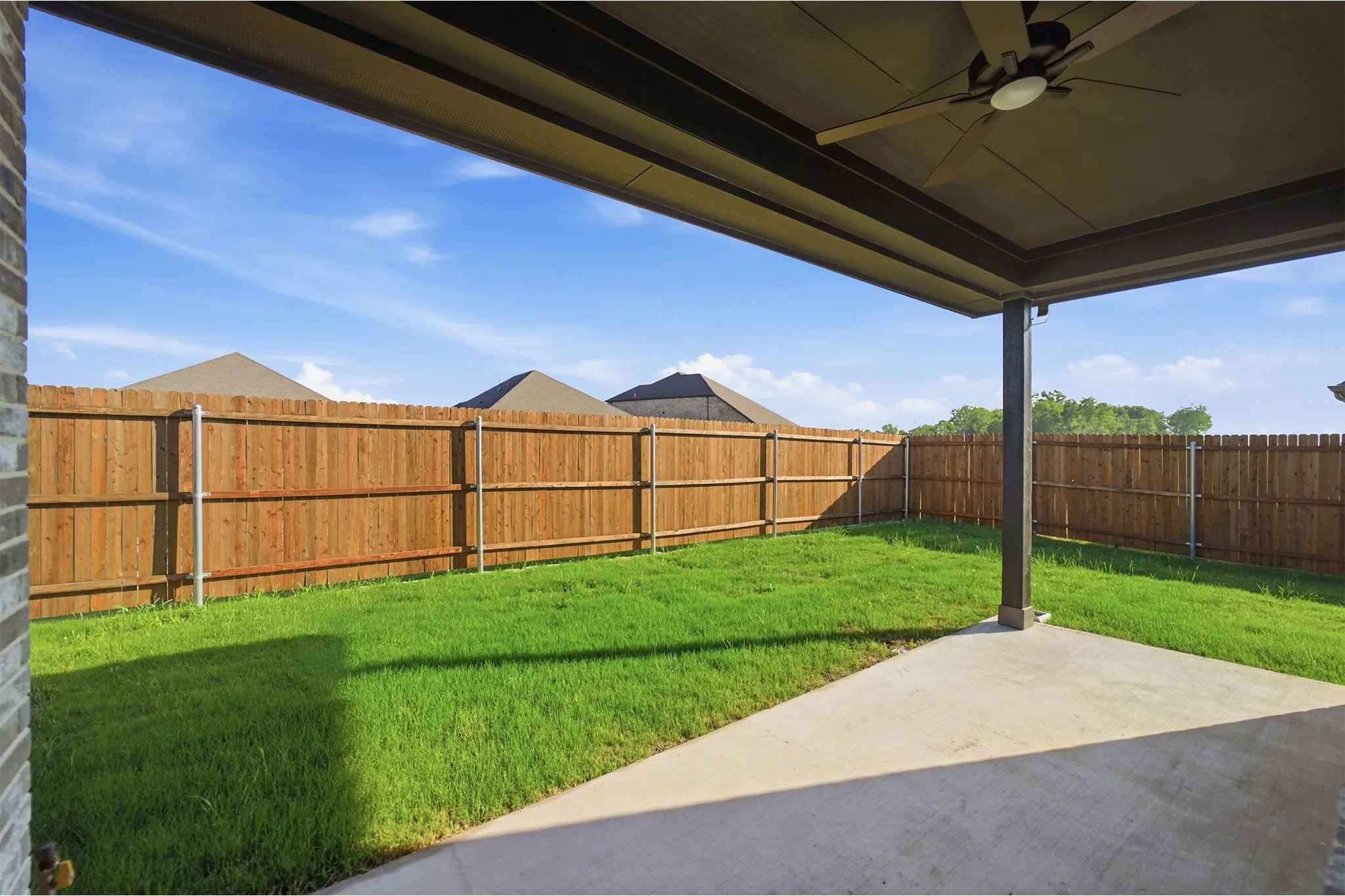 Covered outdoor patio with a ceiling fan, concrete flooring, and a private wooden fence