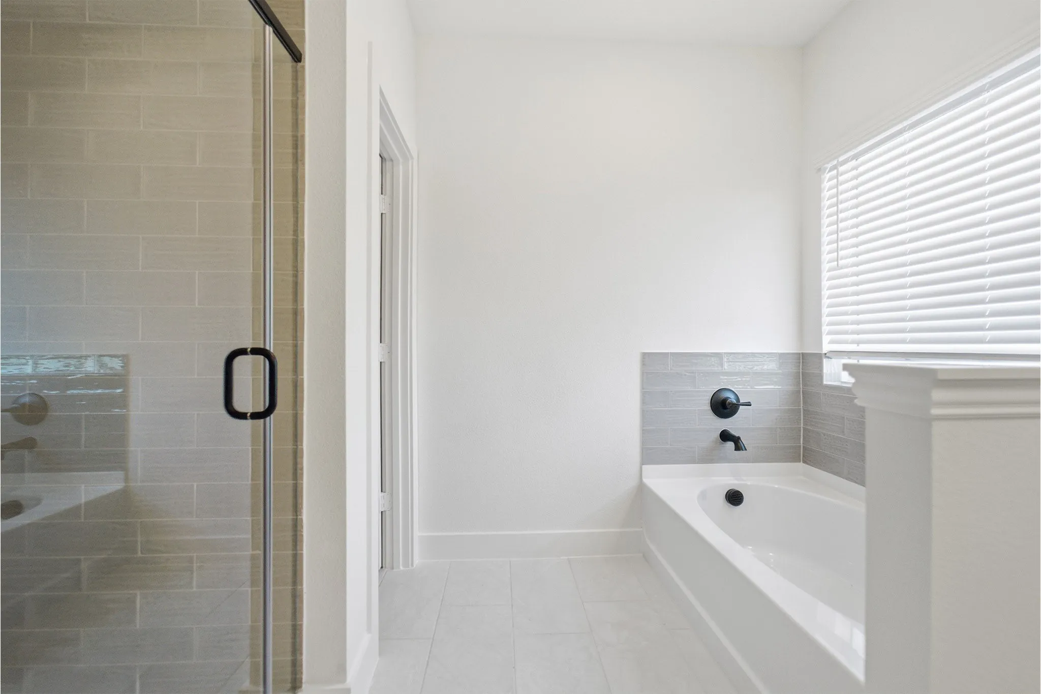 Bathroom featuring a frameless glass shower enclosure, a soaking tub with dark-finish fixtures, and light-toned tile flooring