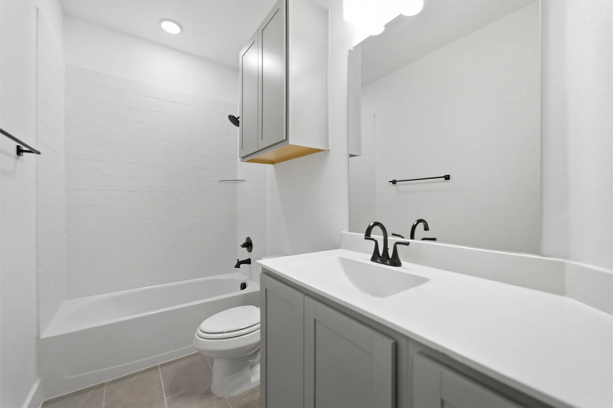 Bathroom featuring a white tub with subway tile surround, gray vanity with integrated sink, white countertop, and matte black fixtures