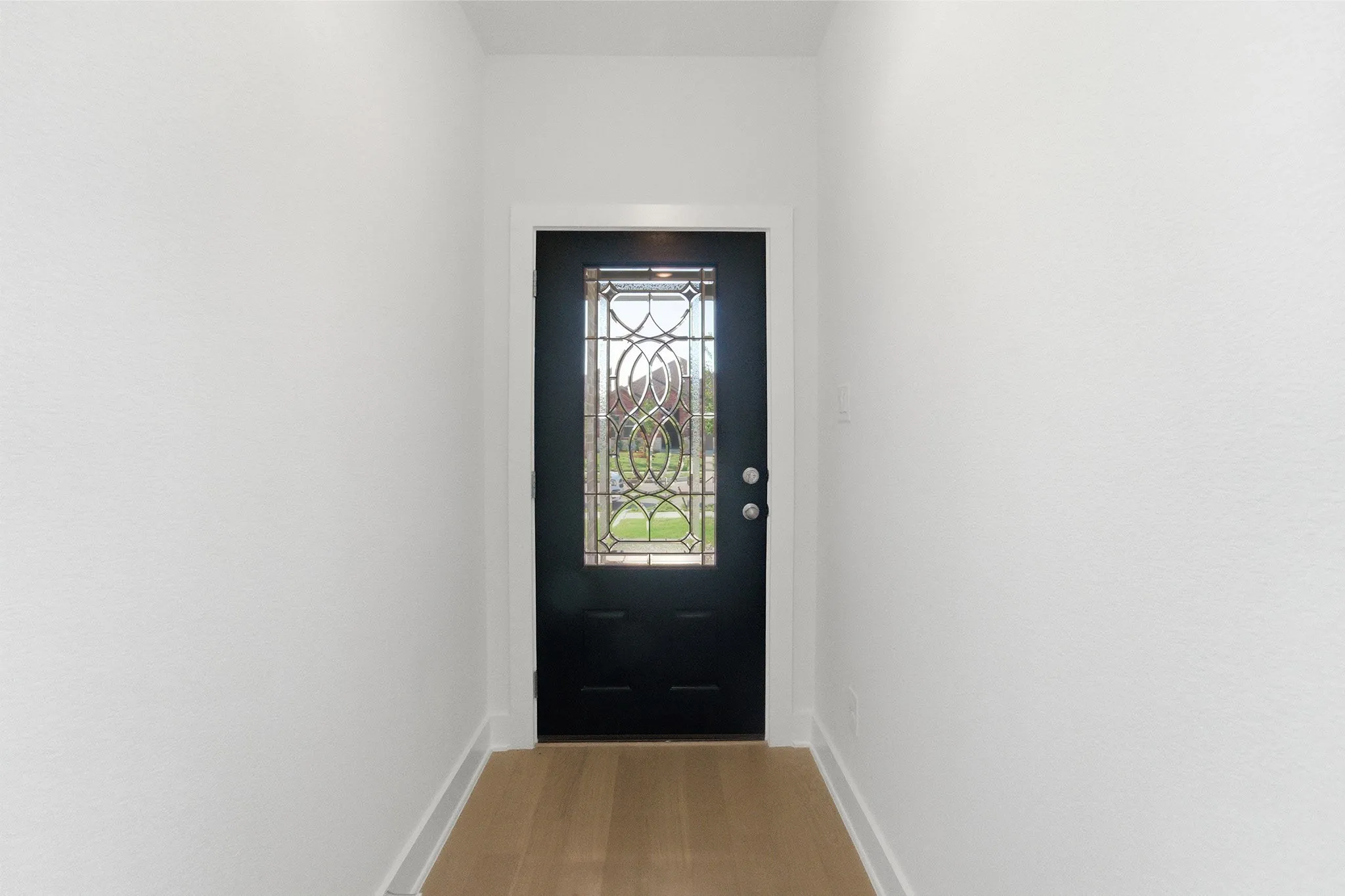 Entryway featuring a black door with decorative glass, wood-finish flooring, and white trim