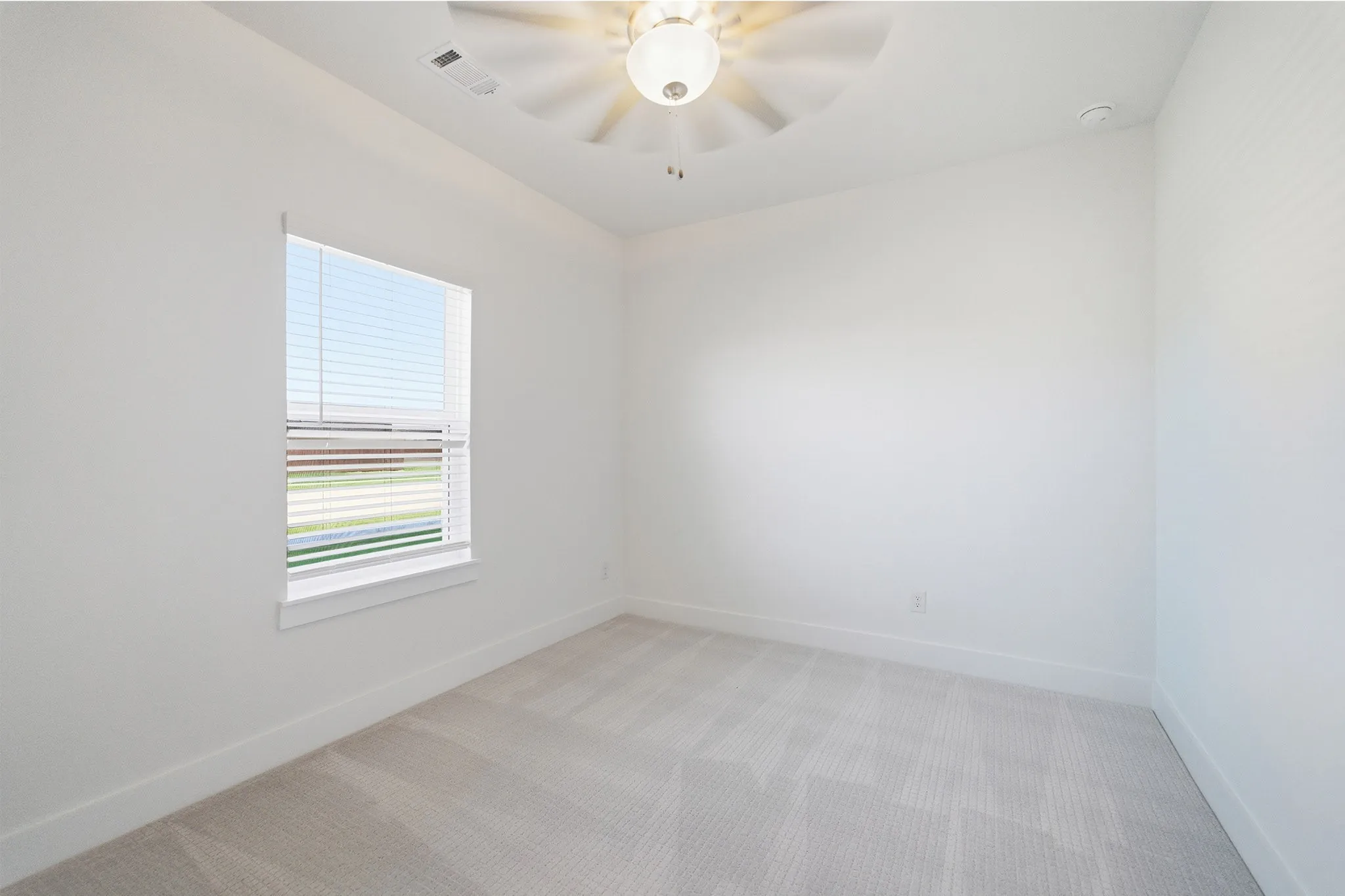 Bright room featuring a single window with blinds, light-toned carpeting, white walls, and a ceiling fan with integrated lighting