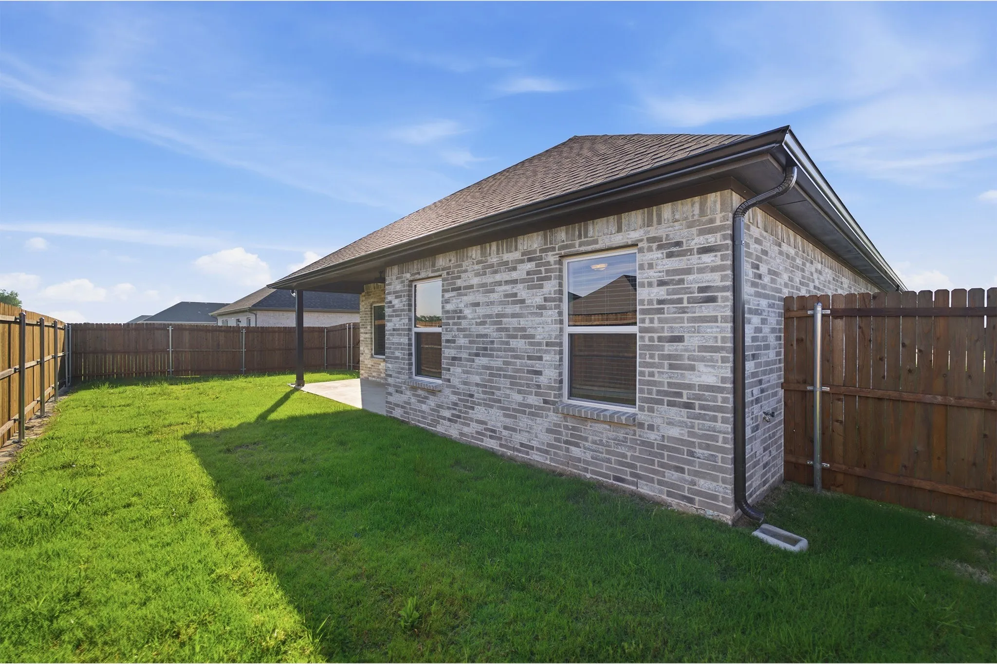 Expansive backyard featuring a manicured lawn, full wood fencing, and a covered concrete patio